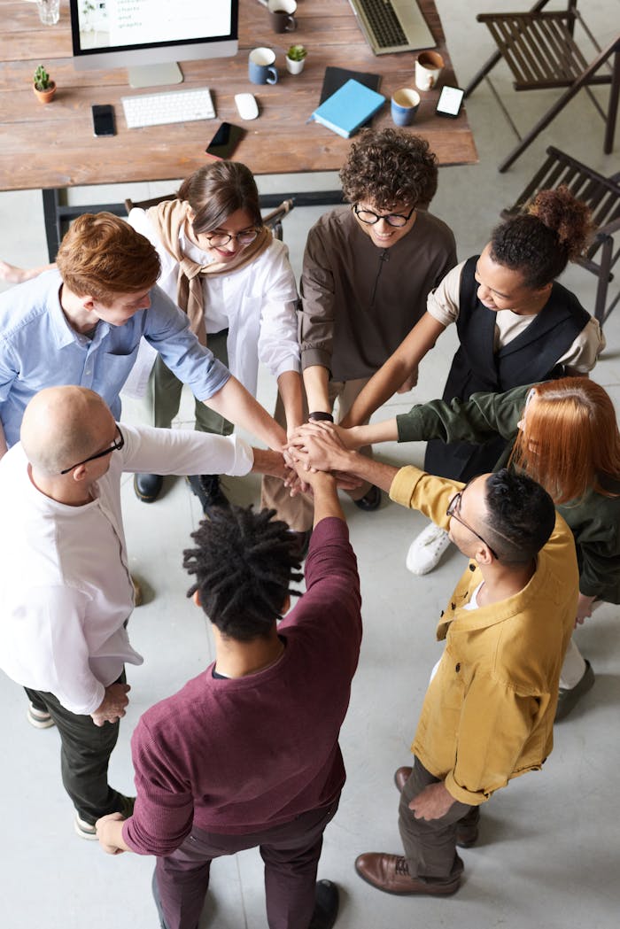 contact-img A diverse group of professionals joins hands in a team-building exercise indoors.