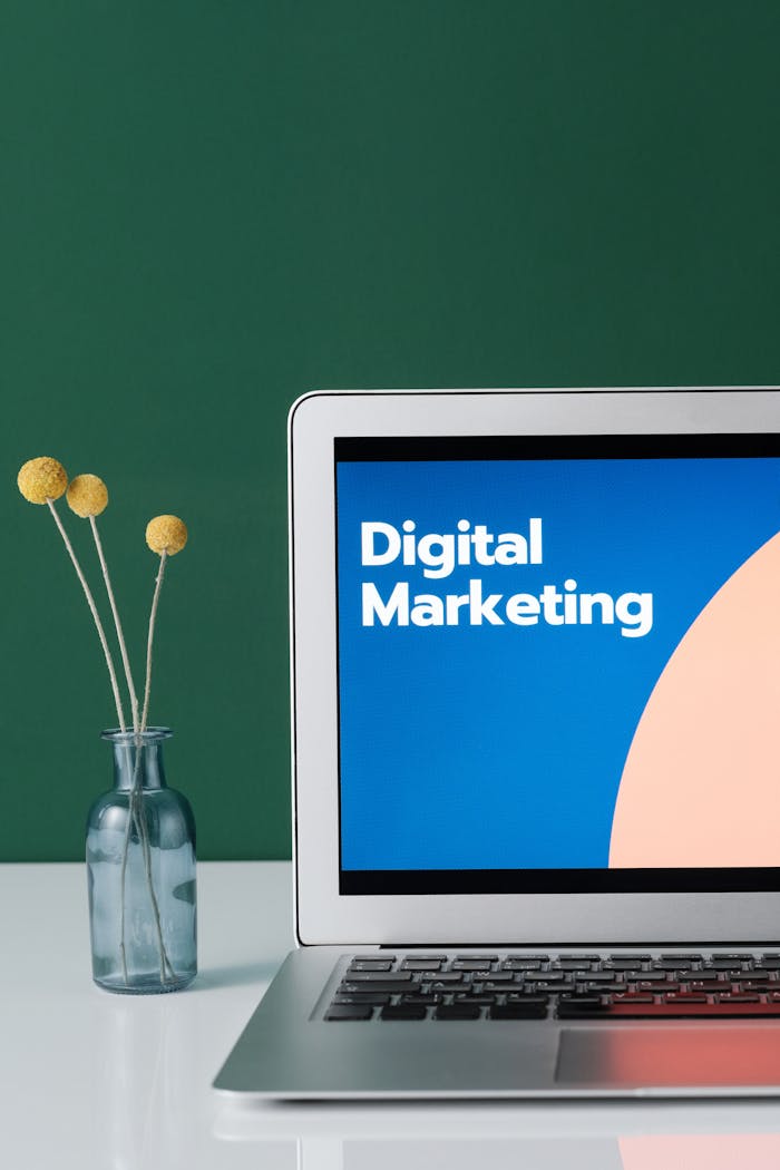 hero-img A laptop displaying 'Digital Marketing' with a minimalist floral decor in a glass vase.
