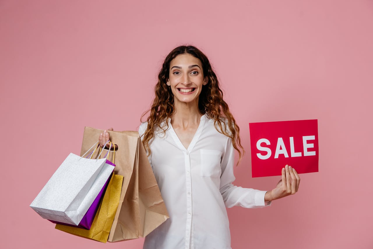 service-02 Smiling woman holding shopping bags and sale sign against pink background in studio.